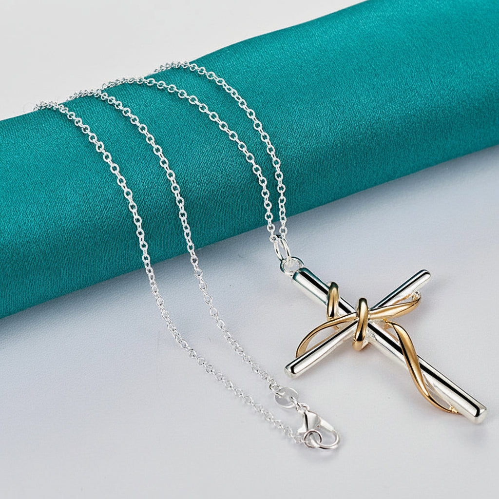 Necklace with a gold and silver cross pendant on a teal fabric background