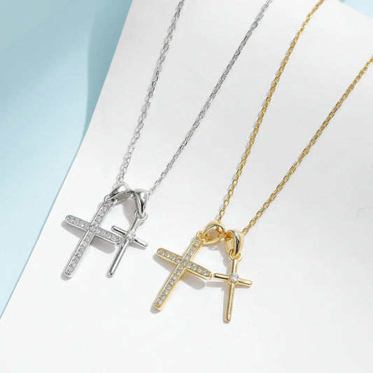 Two cross-shaped necklaces in gold and silver on a light blue background