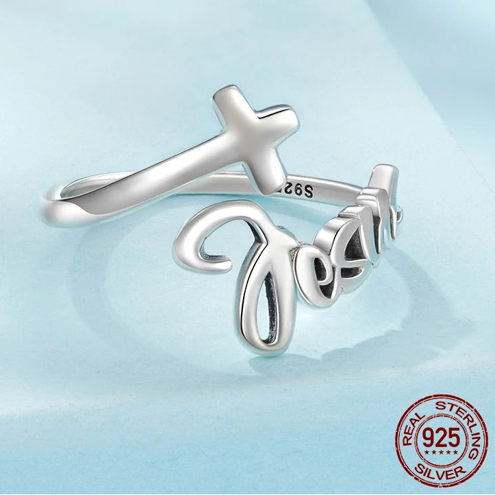Silver ring with cross and 'Jesus' engraving on a light blue background