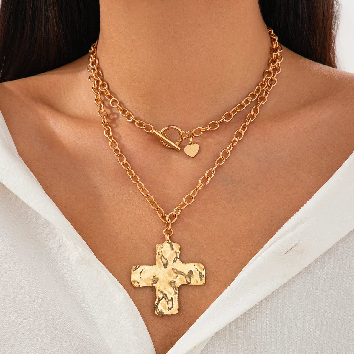 Gold chain necklace with a cross pendant worn by a person against a white background
