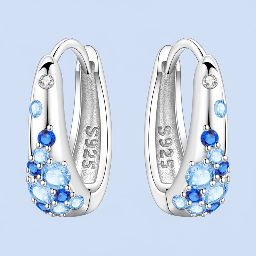 Silver hoop earrings with blue gemstones on a light blue background