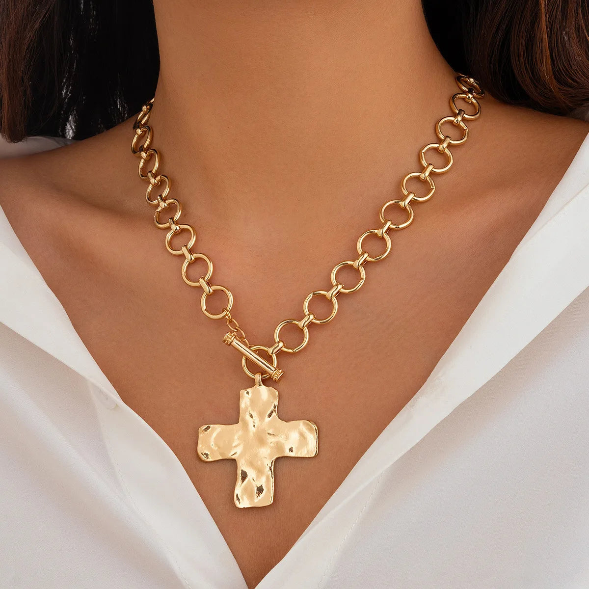 Gold chain necklace with a cross pendant on a person wearing a white top.