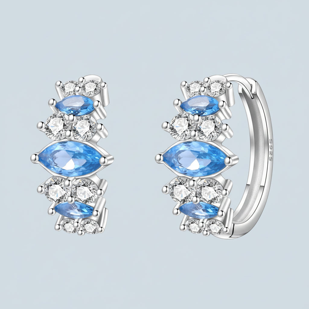 Silver hoop earrings with blue gemstones and clear stones on a light blue background