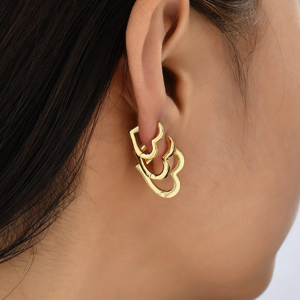 Gold earring worn on an ear with a neutral background
