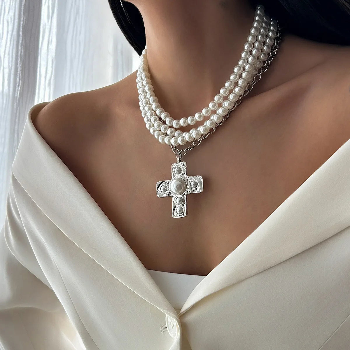 Pearl necklace with a cross pendant worn by a person in a white outfit.
