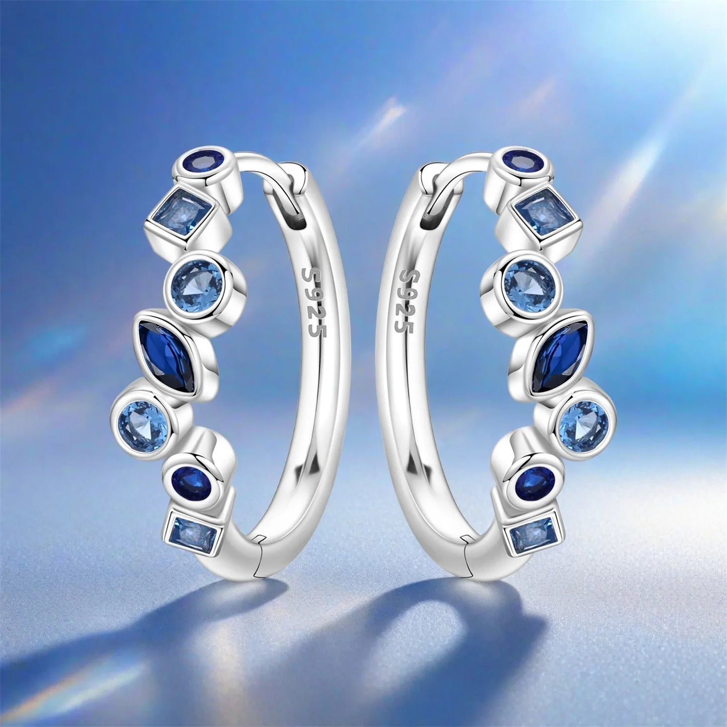Silver hoop earrings with blue gemstones on a blue background