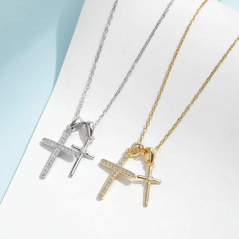 Two cross-shaped necklaces in gold and silver on a light blue background