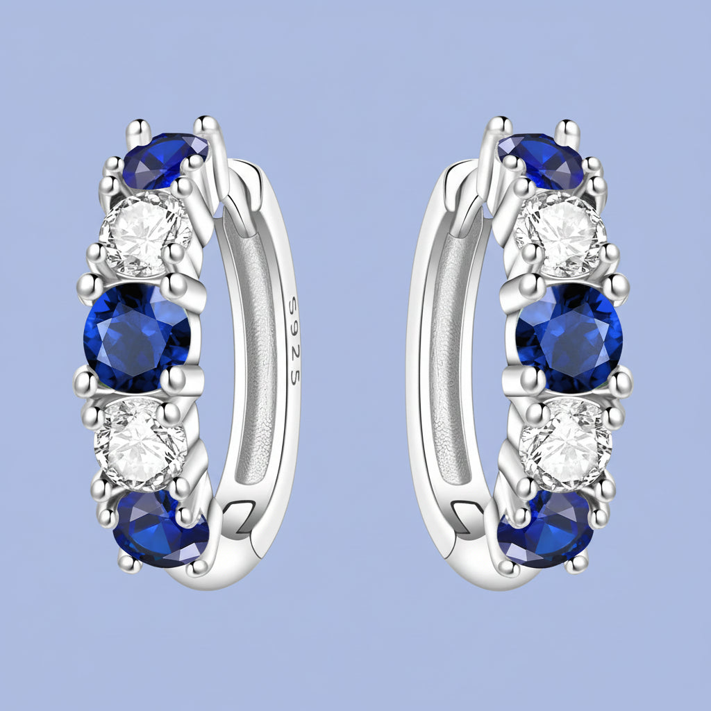 Silver hoop earrings with blue gemstones and clear stones on a light blue background