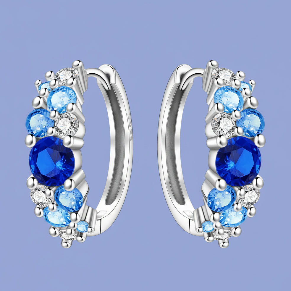 Silver hoop earrings with blue gemstones on a light blue background
