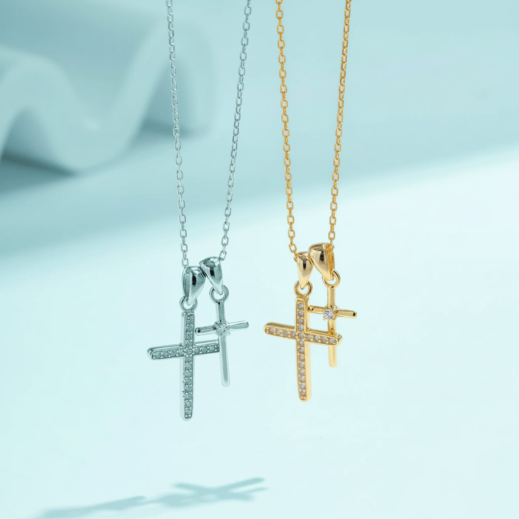 Two cross-shaped pendants on chains, one silver and one gold, against a light blue background.