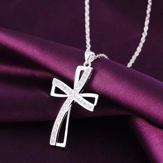 Silver cross pendant necklace on a purple fabric background