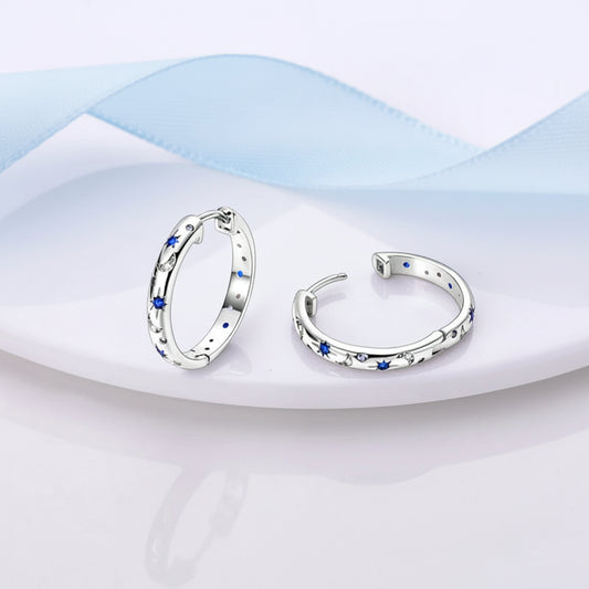 Pair of silver hoop earrings with blue stones on a pink and white fabric background