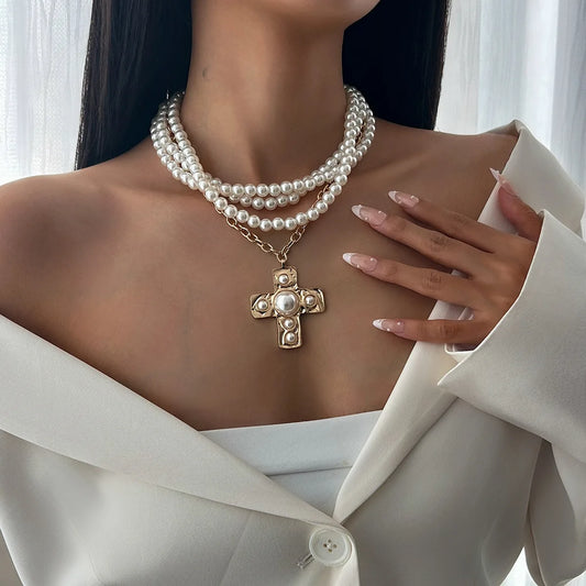 Woman wearing a pearl necklace with a gold cross pendant, holding a white blouse.