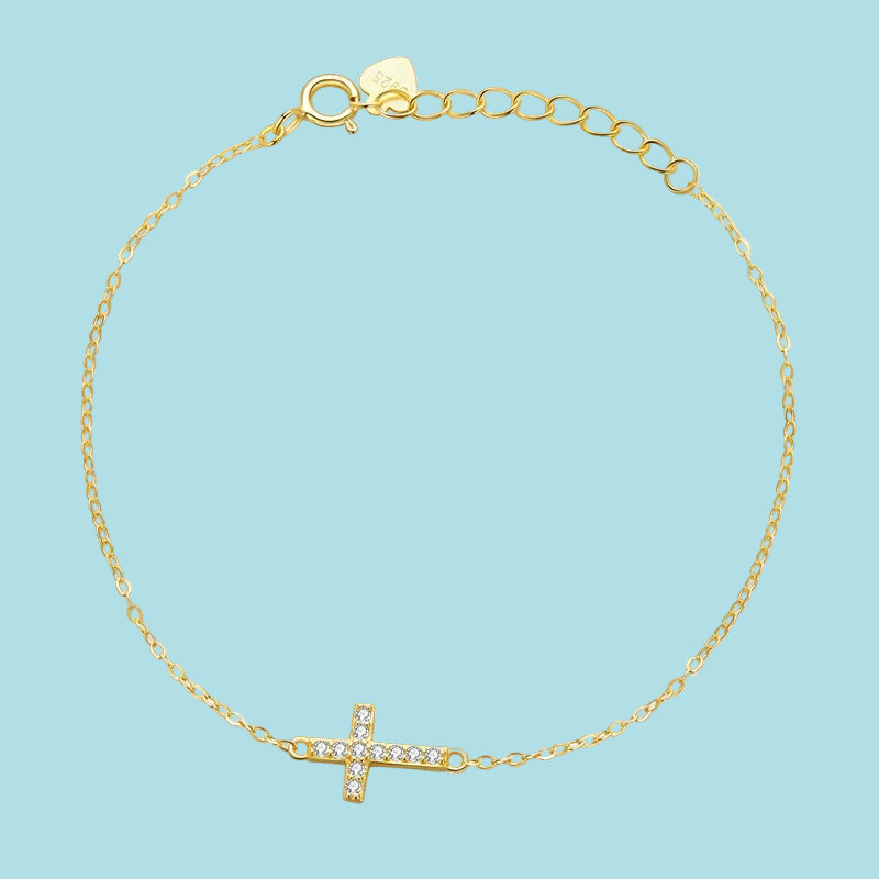 Gold bracelet with a small cross charm on a blue background