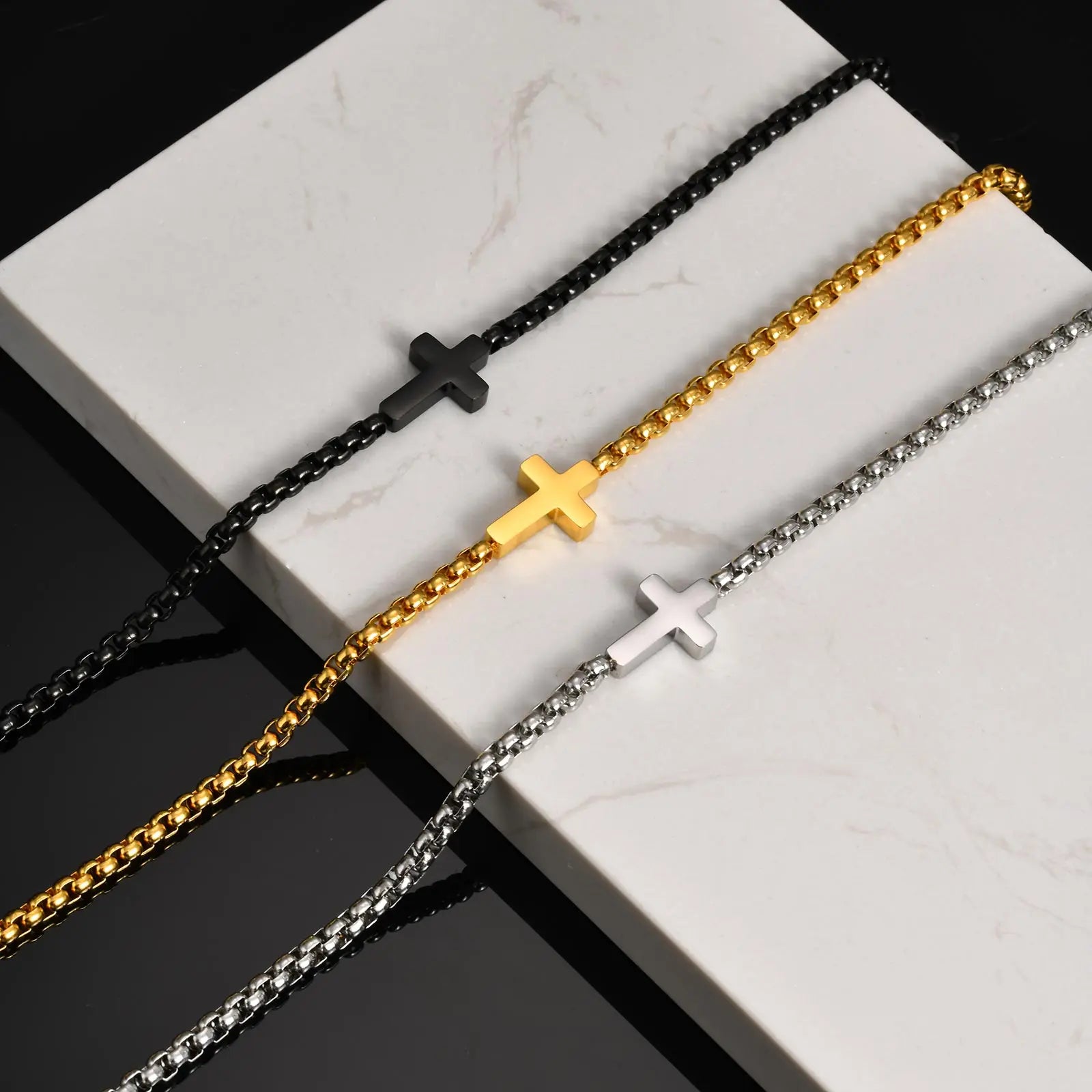 Three chain necklaces with cross pendants on a marble surface