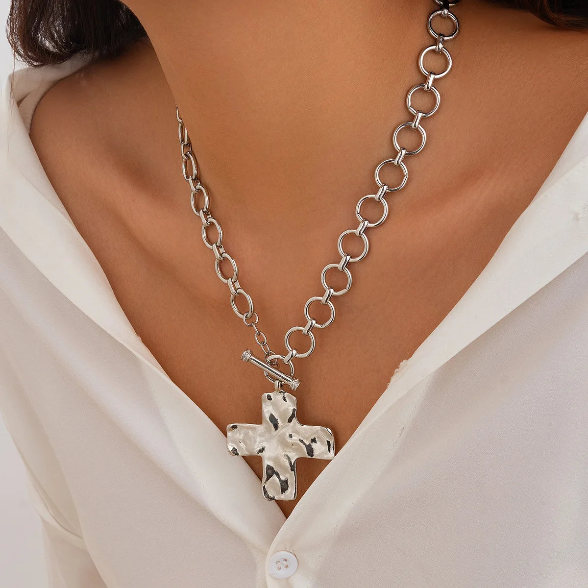 Silver chain necklace with a cross pendant worn by a person in a white shirt.