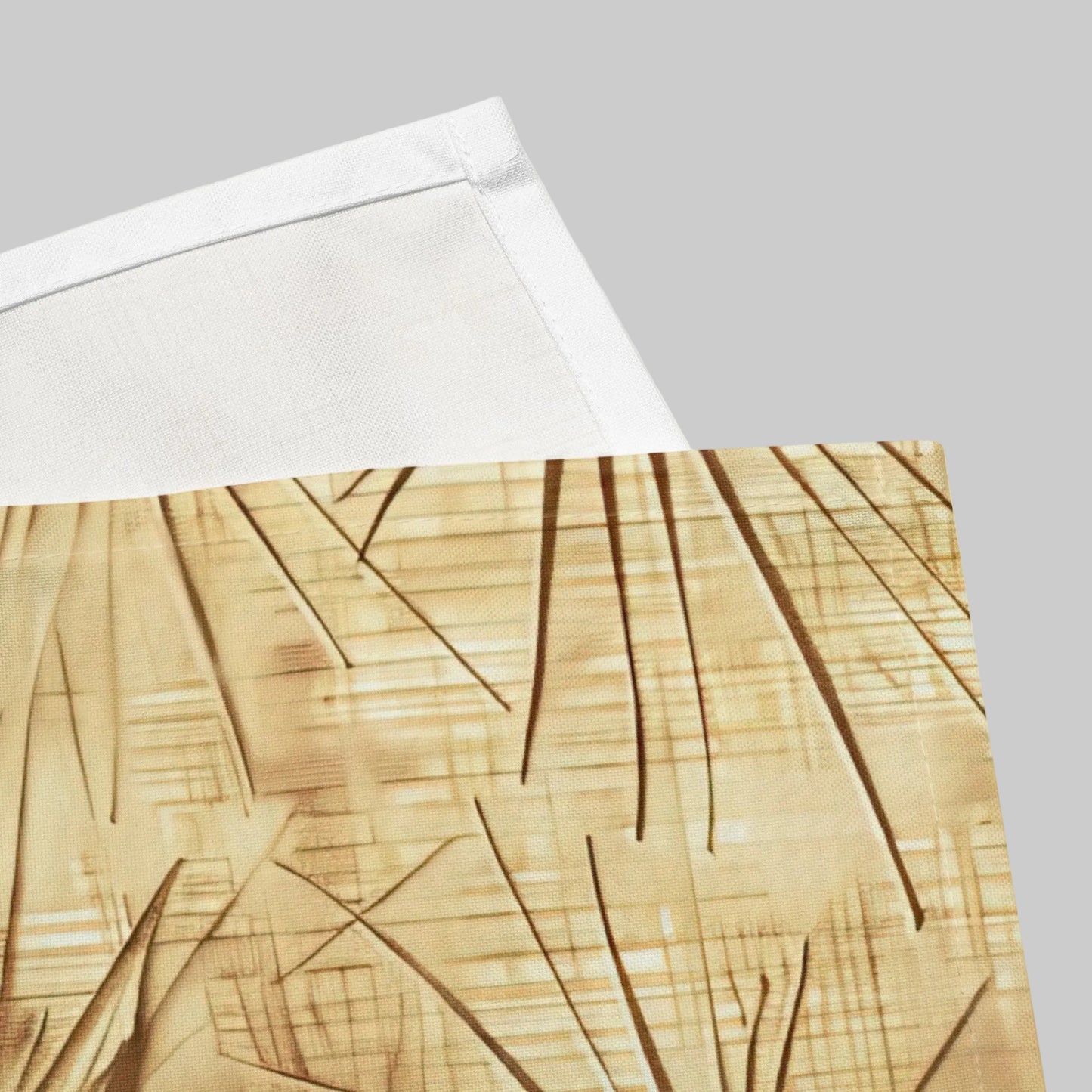 A close-up of a folded textile product, likely a napkin showing a beige and gold abstract pattern with diagonal line details and a white folded edge on a white background.