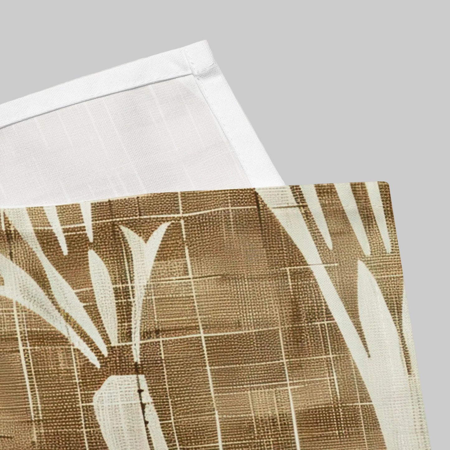 A close-up of a woven textile with a brown and cream abstract botanical pattern, folded over a plain white fabric background.