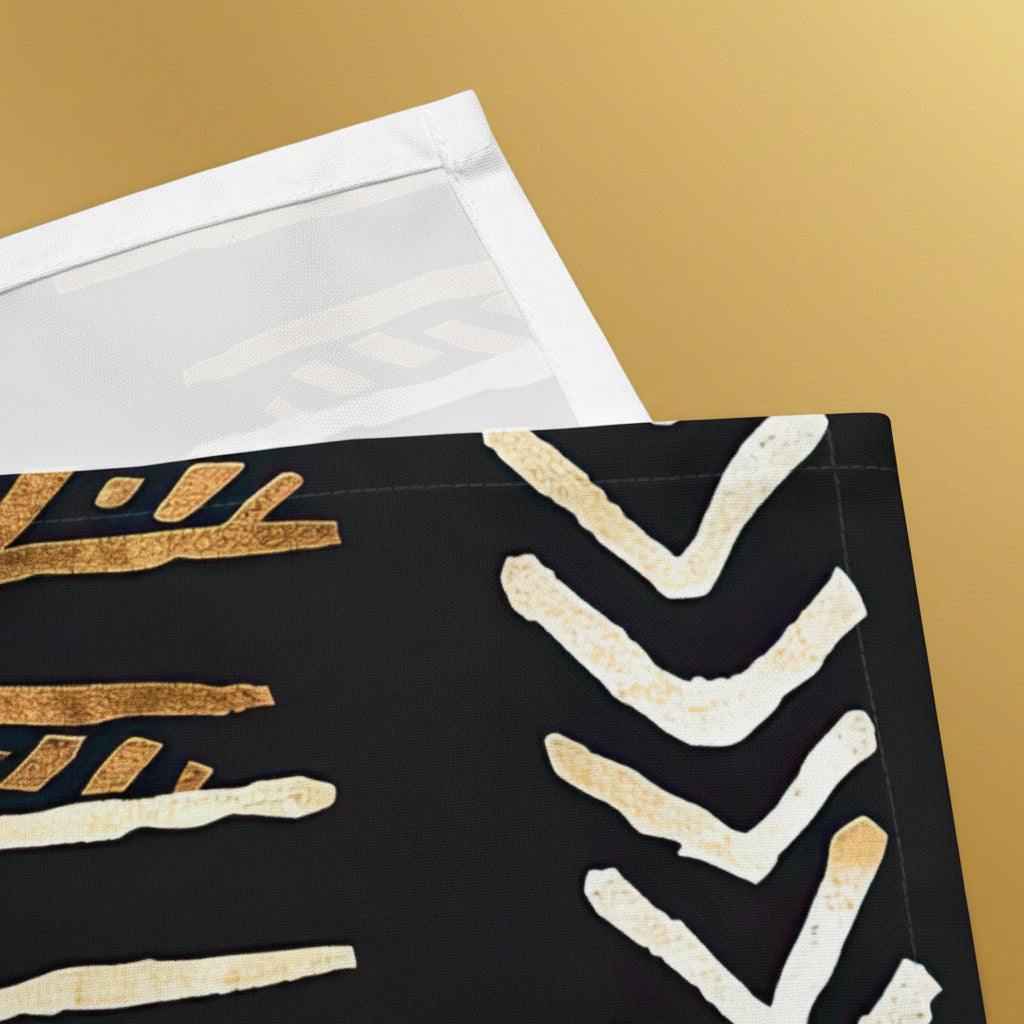 A close-up of a black textile or fabric panel with a pattern of textured gold and off-white chevron and brushstroke motifs, partially folded over with a white backing or sheet visible at the top on a white background.