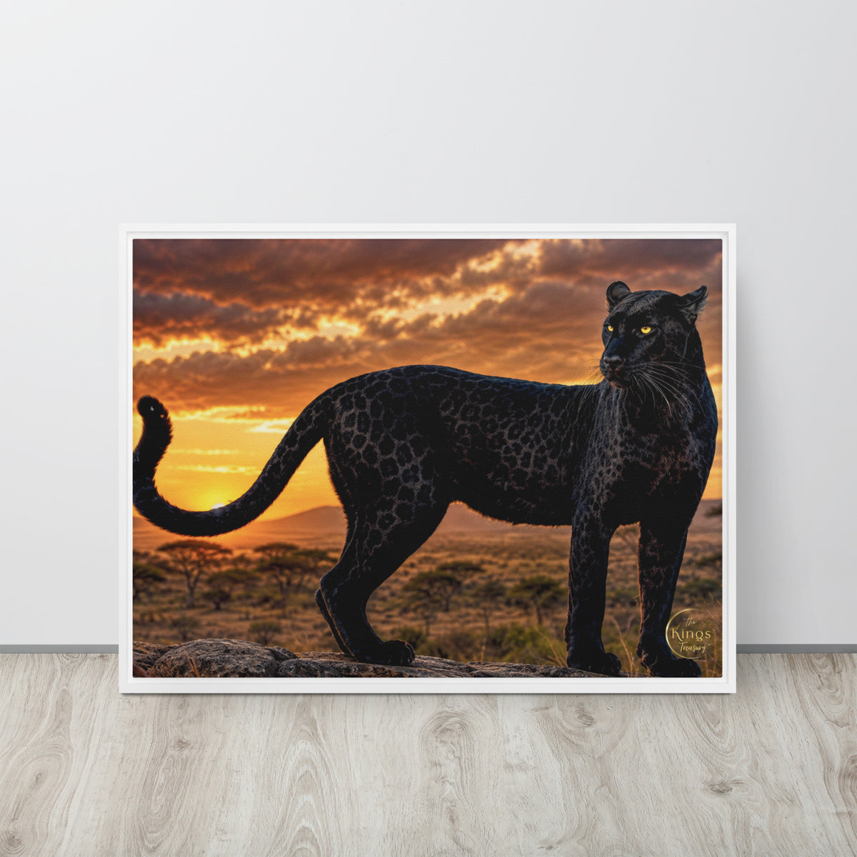 A framed art print of a black leopard standing in a savanna landscape at sunset, leaning against a white wall on a light wood floor.